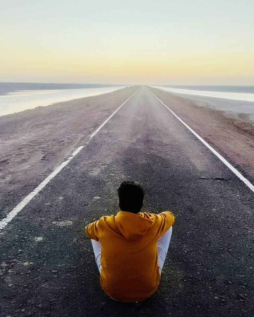 Traveler sitting on the Road to Heaven in Dholavira, Rann of Kutch, surrounded by salt desert and water during sunset.