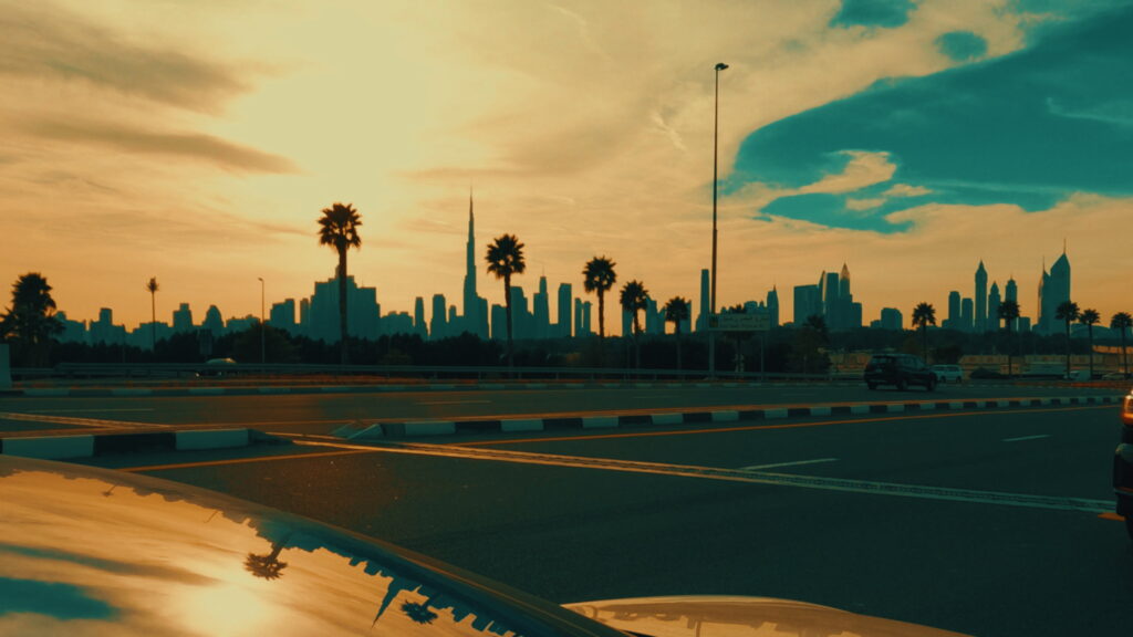 Cinematic sunset view of the Dubai skyline silhouette, featuring the Burj Khalifa in the center, flanked by skyscrapers and palm trees along the highway.